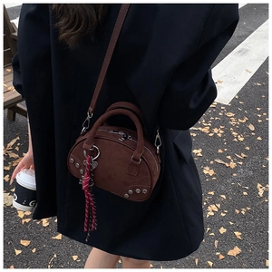 Detail of dark brown suede handbag with fringe heart charm on autumn street