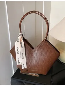 Brown woven tote bag with V-shaped opening and white ribbon decoration on black pedestal