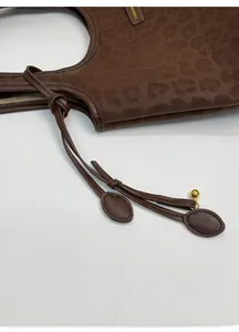 Detail of dark brown leopard print tote bag featuring a decorative leather charm