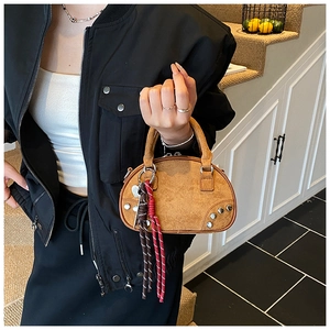 Detail of mini brown faux suede handbag with silver rivets and woven tassel charm