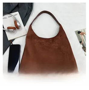 Flat lay of a brown suede hobo tote bag with wide strap and daily lifestyle items