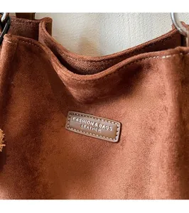 Detailed view of brown suede tote bag with leather logo patch and metal handle rings