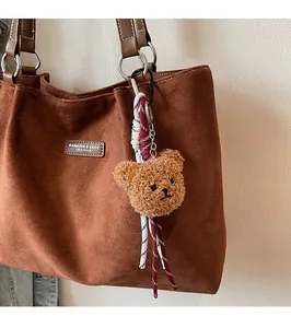 Brown curly plush bear keychain with woven cord on a suede tote bag detail