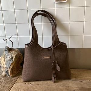 Detail of coffee brown leopard print tote bag with gold metal logo on wooden surface