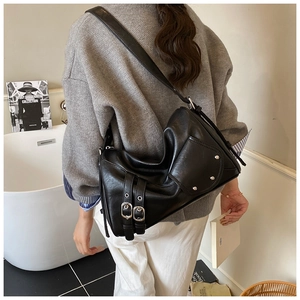 Détail du sac bandoulière en cuir noir avec boucles, rivets argentés et poche latérale