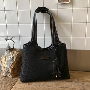Detailed macro view of black leopard print tote with golden metal logo and fringe tassel