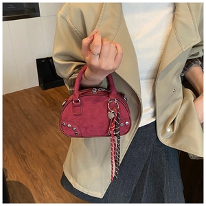 Detail of burgundy suede half-moon bag with silver rivets and heart charm accessory