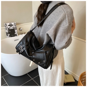 Détail du sac bandoulière noir avec boucles argentées et rivets porté par un mannequin