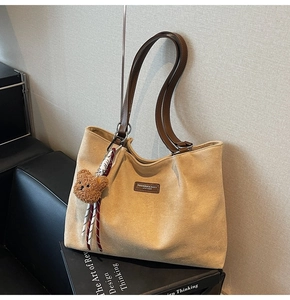 Detail view of khaki suede tote bag with brown leather straps and a plush bear pendant
