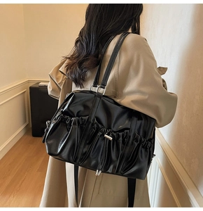 Détail du sac bandoulière plissé mat noir avec cordon sur un modèle en trench-coat