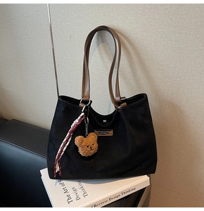 Detail of black suede tote bag featuring brown leather straps and a plush bear pendant