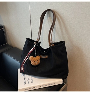 Detail of black suede tote bag with brown leather handles and a cute plush bear pendant