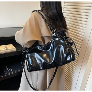 Sac à bandoulière noir brillant avec cordon de serrage et plis, porté par un mannequin