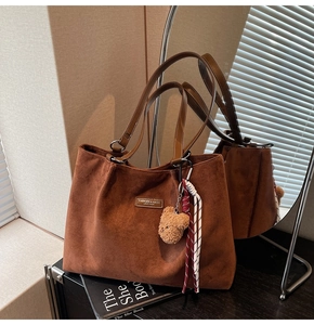 Detail of a brown suede tote bag with a decorative plush bear and branded metal plate