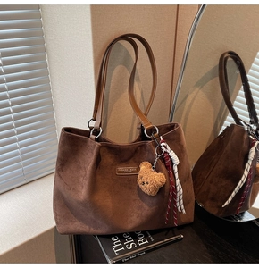 Detail of suede tote bag featuring metallic fashion logo and cute plush bear charm