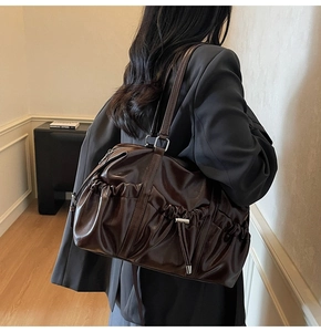 Détail d'un sac cabas en cuir verni marron foncé avec plis élégants et cordons sur les côtés