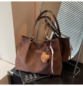 Brown suede tote bag with teddy bear charm and woven rope detail on a stack of books