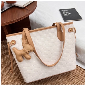White checkered tote bag with brown leather handles and cute dog charm on woven carpet
