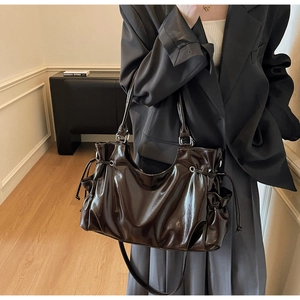 Détail d'un sac cabas marron brillant avec cordons latéraux et détails métalliques