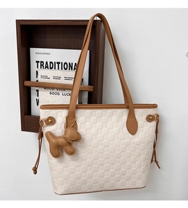 Detail of beige woven tote bag with brown leather handles and a puppy-shaped charm