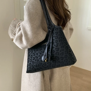 Shoulder shot of a leopard print tote bag with gold charm and black leather strap