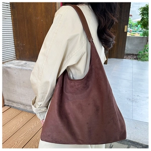 Detail of a dark brown suede tote bag featuring smooth leather straps and matte texture