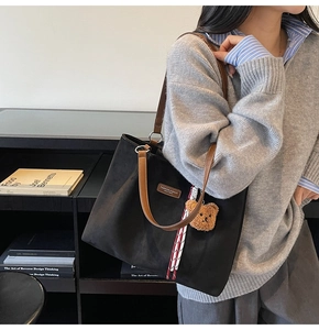Detail view of black suede tote bag featuring brown leather handles and a plush bear charm
