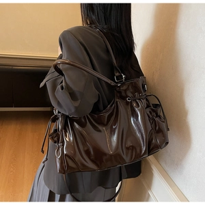 Detail of dark coffee patent leather shoulder bag with side drawstring and metal buckles