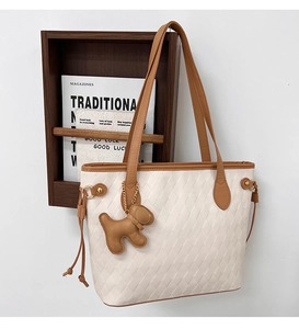 Detail of off-white quilted tote bag with caramel trim and cute puppy charm accessory
