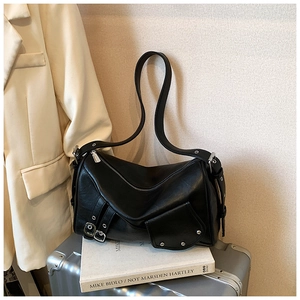 Détail d'un sac cabas noir en cuir PU plissé avec rivets posé sur une valise argentée