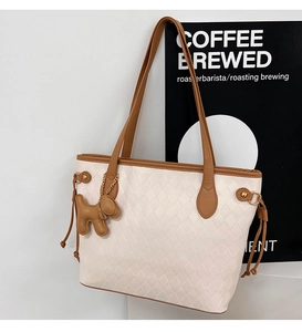 Macro detail of cream quilted tote bag with brown dog charm and metal ring accents