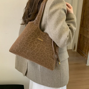Detail of a brown leopard print tote bag with a golden metal logo on suede texture
