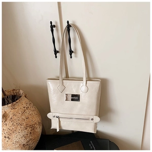 Détail d'un sac cabas blanc crème en cuir verni plissé avec une plaque de marque métallique