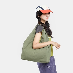 Side view of an olive green nylon tote bag worn by a model in a minimalist setting