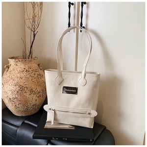 Détail du cabas en cuir verni plissé beige avec plaque métallique et logo gravé