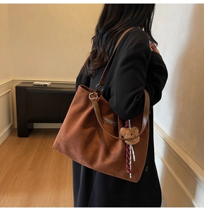 Brown suede tote bag with leather straps and bear pendant shown on model in black suit