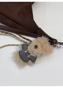 Detail of cute teddy bear plush charm with woven lanyard on a brown suede tote bag