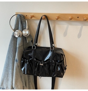 Detail view of the black pleated tote bag showing the drawstring clasp and side pockets