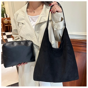 Close-up of black suede tote bag and leather clutch set shown in a lifestyle scene