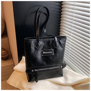Gros plan du sac cabas noir avec texture en similicuir plissé et plaque métallique logo