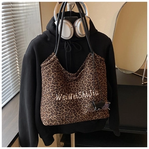 Detail of leopard print tote bag featuring white embroidery and slim black leather handles