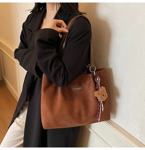 Detail of brown suede tote bag with leather strap and plush bear charm for daily commute