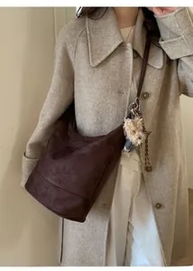 Detailed shot of brown suede tote bag featuring plush puppy charm and woven rope accent
