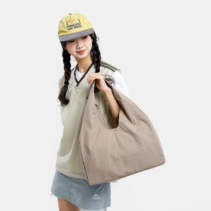 Side view of large khaki nylon crescent tote bag shown on a model in sporty casual style