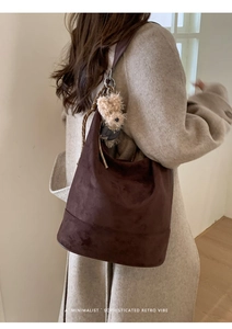 Detail of dark brown suede tote bag featuring a cute plush dog charm on a soft strap