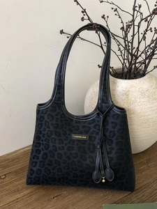 Chic black leopard print tote bag with tassel charms on a rustic wooden surface