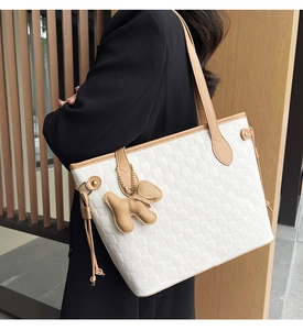Close-up of white woven checkered tote bag with caramel straps and a dog charm accessory