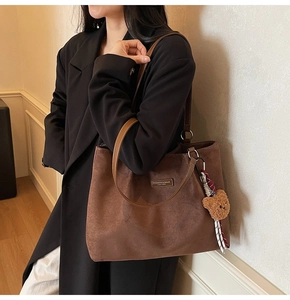 Detail of brown suede tote bag with leather straps and bear charm accessory