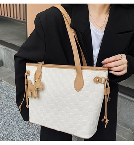 Close-up of a white checkered tote bag with brown leather straps and a cute dog charm