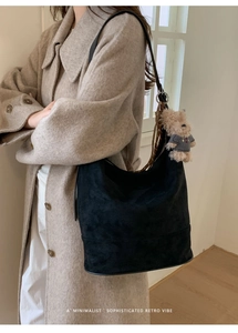 Detail of black suede hobo bag with cute bear charm worn on a stylish beige coat